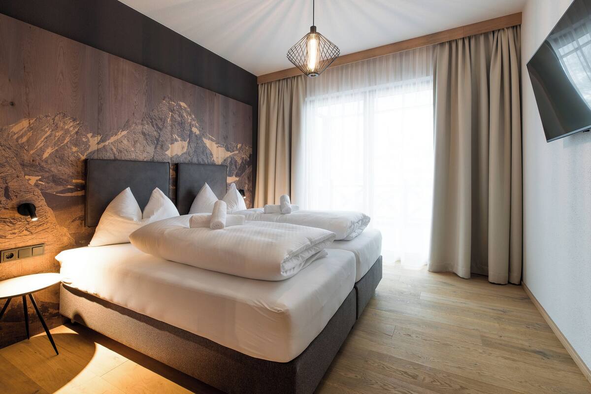 Een moderne hotelkamer met een groot bed, een wandtelevisie en een kunstwerk met een berglandschap.