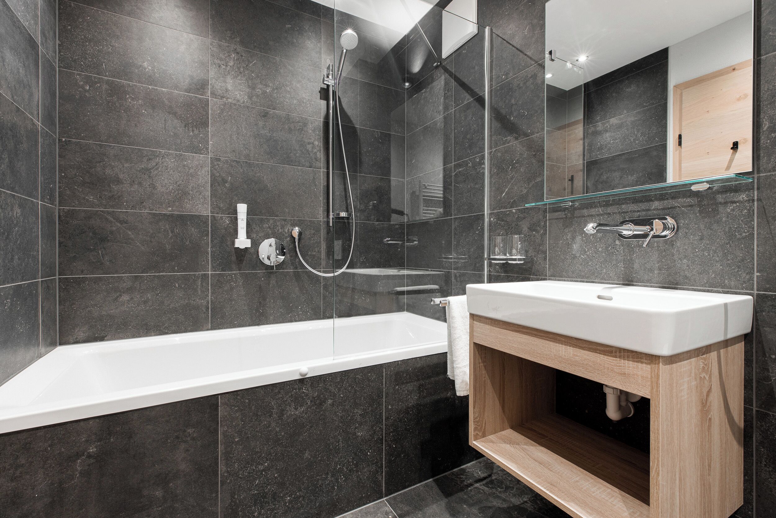 Ein modernes Badezimmer mit einer gläsernen Duschkabine, einer weißen Badewanne und einem Holzbadezimmer-Möbel mit Waschbecken.