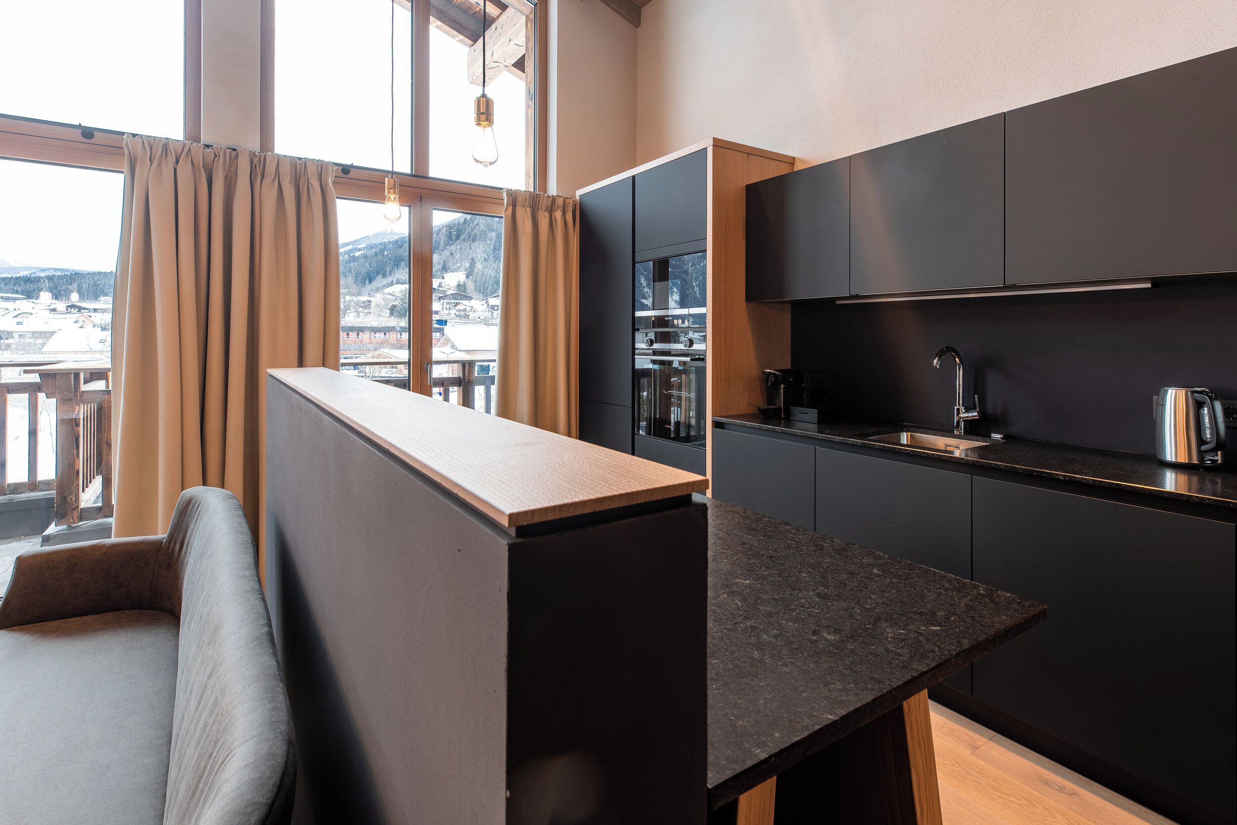 A modern kitchen with dark cabinetry, a wooden countertop, and a view of a snowy landscape through large windows.