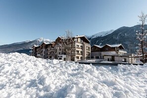 A snow-covered mountain resort with multiple wooden buildings, a ski lift, and a clear view of snow-capped mountains in the background.