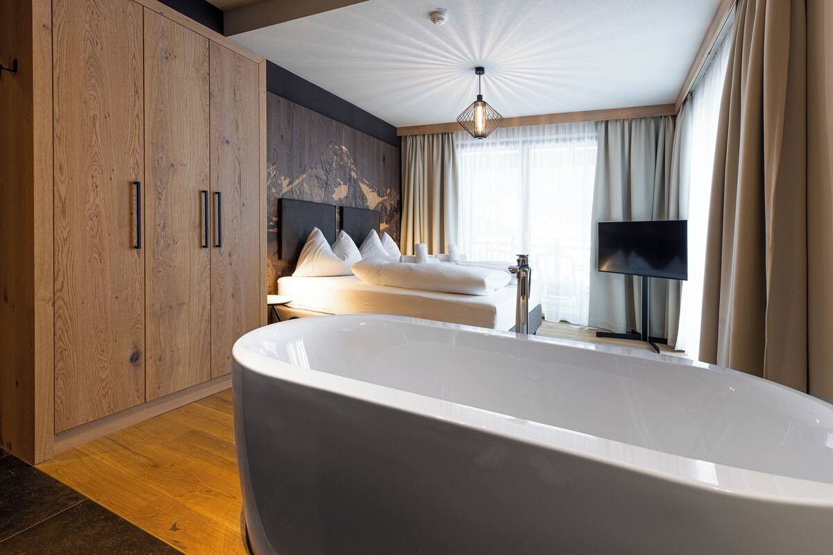 Een moderne hotelkamer met een groot bad, een houten garderobe en een flatscreen televisie.