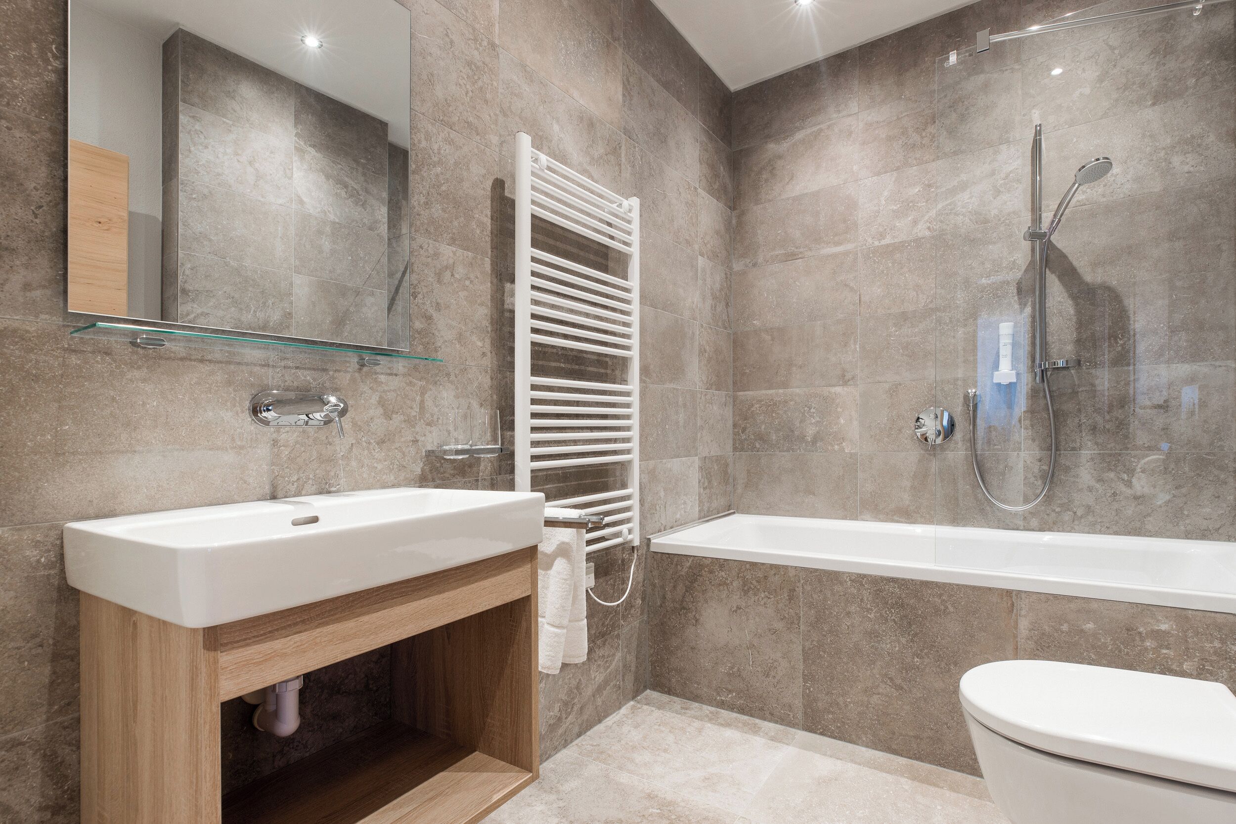 A modern bathroom with a glass shelf, a white sink, a towel rack, a bathtub, and a toilet.