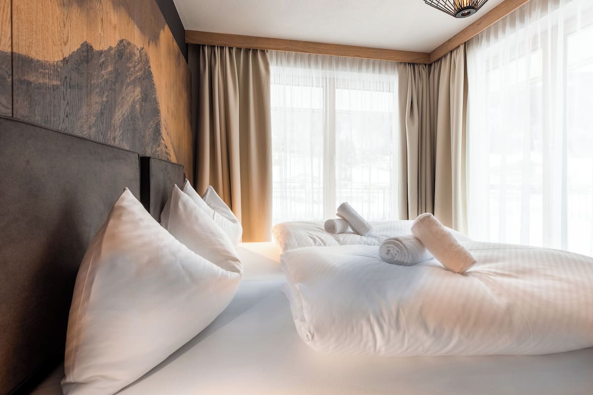 Een hotelkamer met twee bedden, beige gordijnen en een berglandschap op de muur.