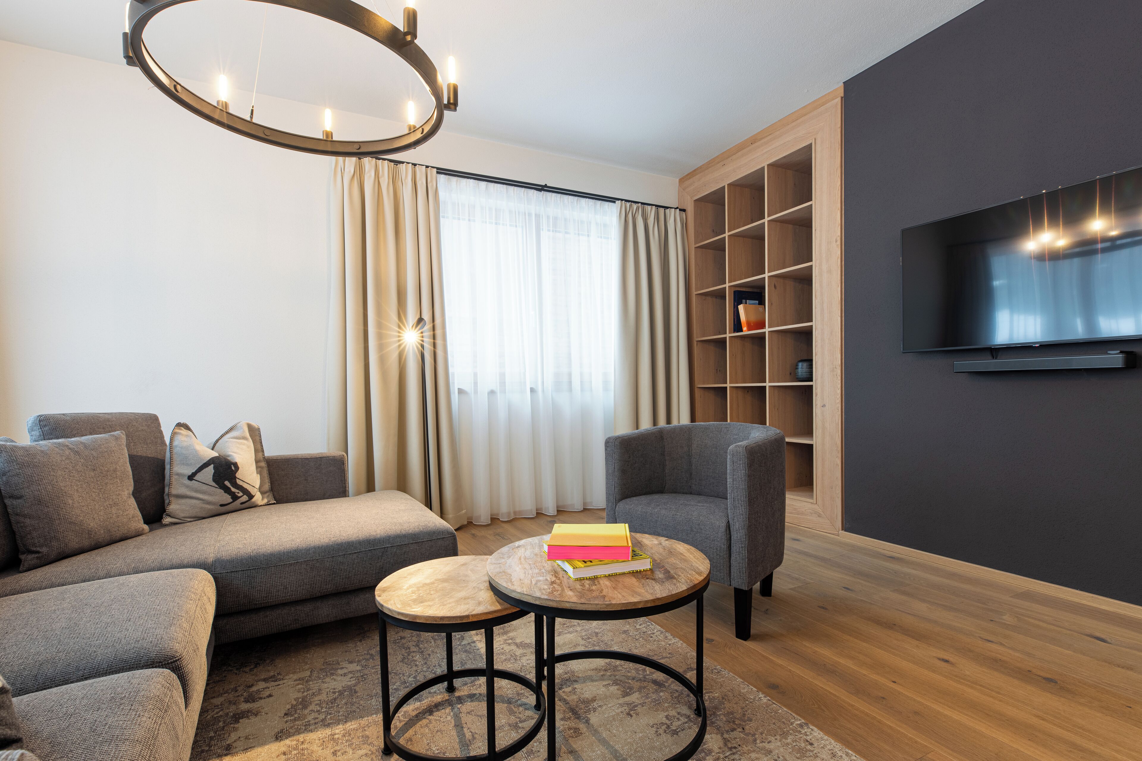 A modern living room with a sofa, armchairs, a coffee table, a TV, and a bookshelf.