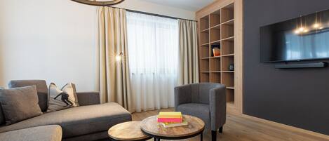Un salon moderne comprenant un canapé, des fauteuils, une table basse, un téléviseur et une bibliothèque.