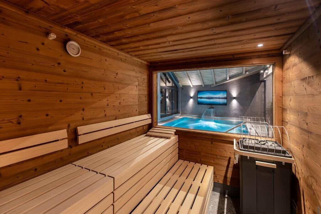 Una sala de sauna con bancos de madera, una bañera de hidromasaje visible y un televisor en la pared.