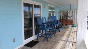 A covered porch with a wooden deck, a bench, and blue Adirondack chairs. - Brower's Lagoon Run at the Beach (Gulf Shores)