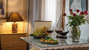 Una mesa con cubierta de vidrio, un florero con rosas rojas, un cuenco de uvas y dos copas de vino tinto.