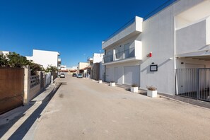 Una estrecha calle urbana bordeada de edificios modernos, con un cielo azul despejado y algunos coches estacionados.