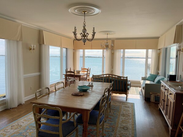 A dining area with a wooden table, chairs, and a view of the water. - Assateague Point - Dynamic Waterfront ,Pier,Dock, LINENS AND TOWELS PROVIDED (Chincoteague)