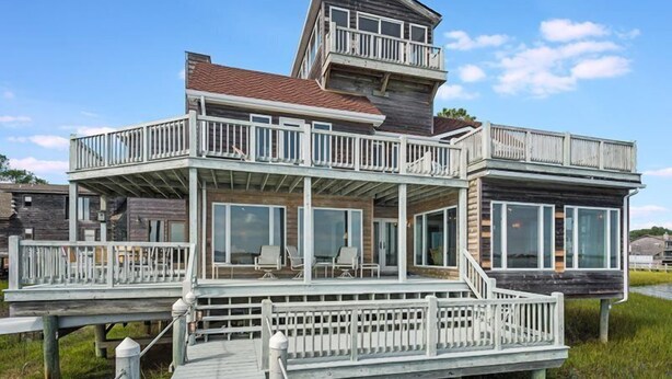 A multi-level wooden house with a balcony, large windows, and a deck. - Assateague Point - Dynamic Waterfront ,Pier,Dock,  LINENS AND TOWELS PROVIDED (Chincoteague)