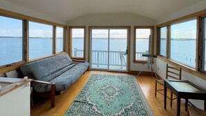 A room with a large window overlooking a body of water, a ceiling fan, a sofa, a small table, and a rug. - Assateague Point - Dynamic Waterfront ,Pier,Dock,  LINENS AND TOWELS PROVIDED (Chincoteague)