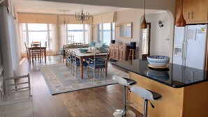 A modern kitchen with a dining area, wooden cabinets, a large island, and a view of the water. - Assateague Point - Dynamic Waterfront ,Pier,Dock,  LINENS AND TOWELS PROVIDED (Chincoteague)