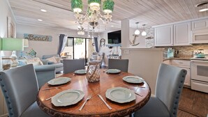 Un comedor con una mesa de madera dispuesta para seis personas, rodeada de sillas tapizadas. Sobre la mesa hay un jarrón decorativo con piedras, y un candelabro cuelga del techo.