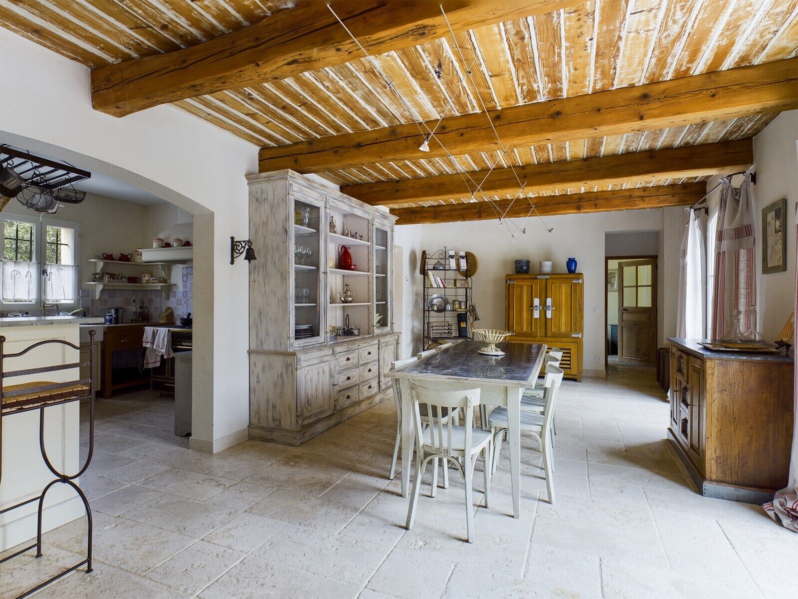 Une cuisine rustique avec des poutres en bois, une table à manger avec des chaises et un grand buffet aux portes vitrées.