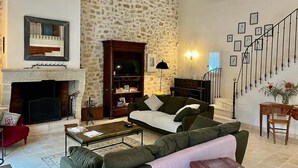 Ein Wohnzimmer mit Steinwand, Kamin, einer Couch, einem Couchtisch und einer Treppe mit gerahmten Bildern.