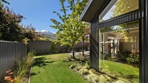 A modern house with a well-maintained garden, large windows, and a view of mountains. - Luxe Arrowtown Holiday Home (Arrowtown)