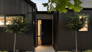 A modern building with a dark facade, a central entrance, and two potted trees on either side. - Luxe Arrowtown Holiday Home (Arrowtown)
