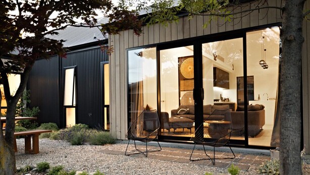 A modern house with a large glass door leading to a living area with a sofa and chairs. - Luxe Arrowtown Holiday Home (Arrowtown)
