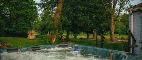 A hot tub in a backyard with trees and a house in the background.