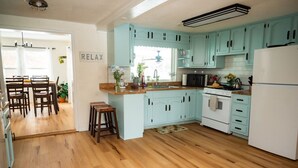 A kitchen with light blue cabinets, a wooden floor, a white refrigerator, and a dining area with a table and chairs. - LAKEHOUSE/HOT TUB/8 MILES TO DOWNTOWN/ON 60 ACRES (Indianapolis)
