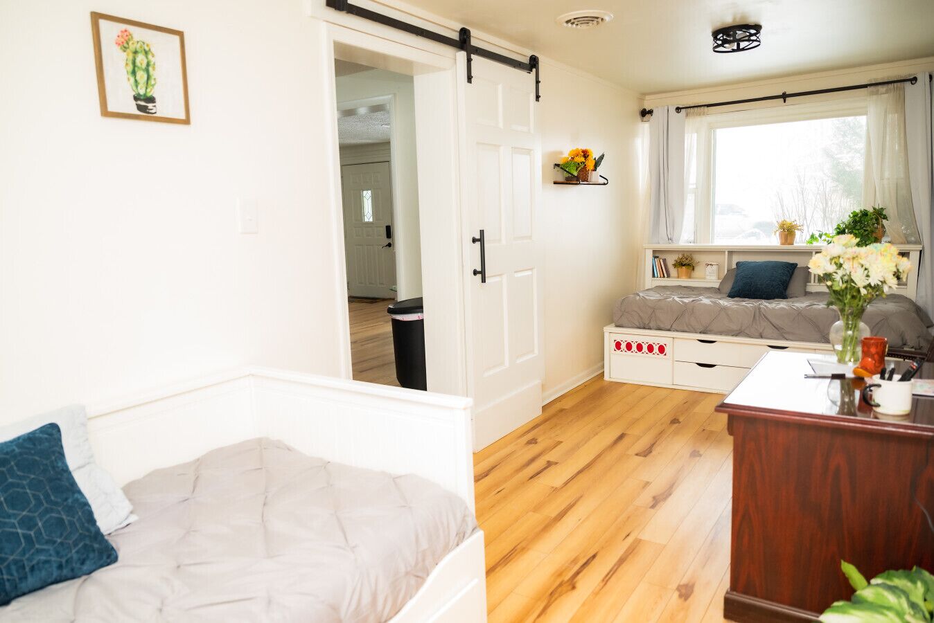 A room with a bed, a desk, and a window with curtains. There is a door leading to another room.