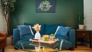 A living room with a blue sofa, a glass coffee table, and a green wall with a 'gather' sign. - LAKEHOUSE/HOT TUB/8 MILES TO DOWNTOWN/ON 60 ACRES (Indianapolis)