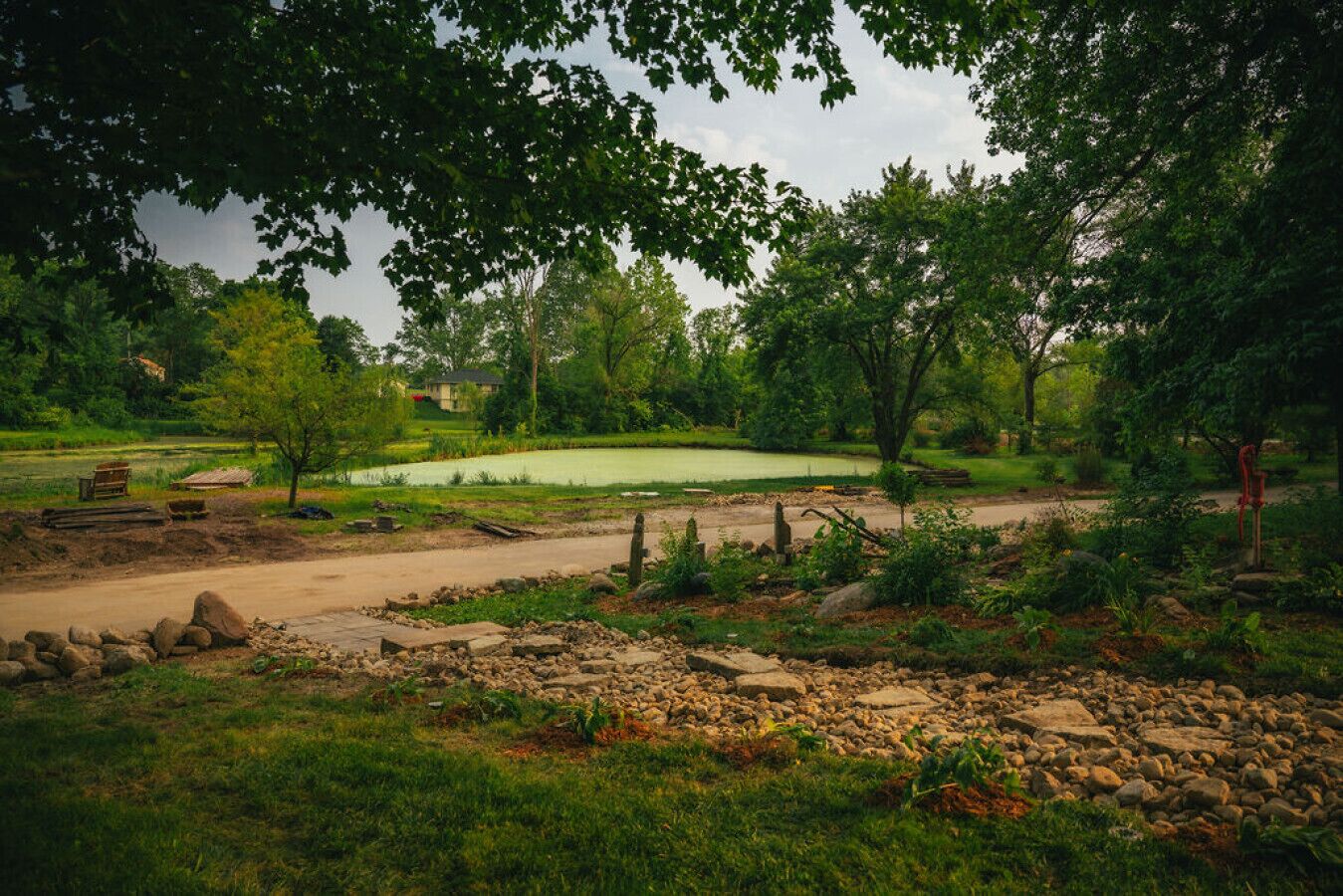 A golf course with a pond, surrounded by trees and a dirt path.