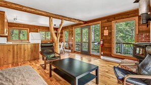 A spacious living area with wooden floors, a black coffee table, leather chairs, a fireplace, and large windows offering views of the surrounding forest. - Mersey River Chalets a nature retreat (Maitland Bridge)