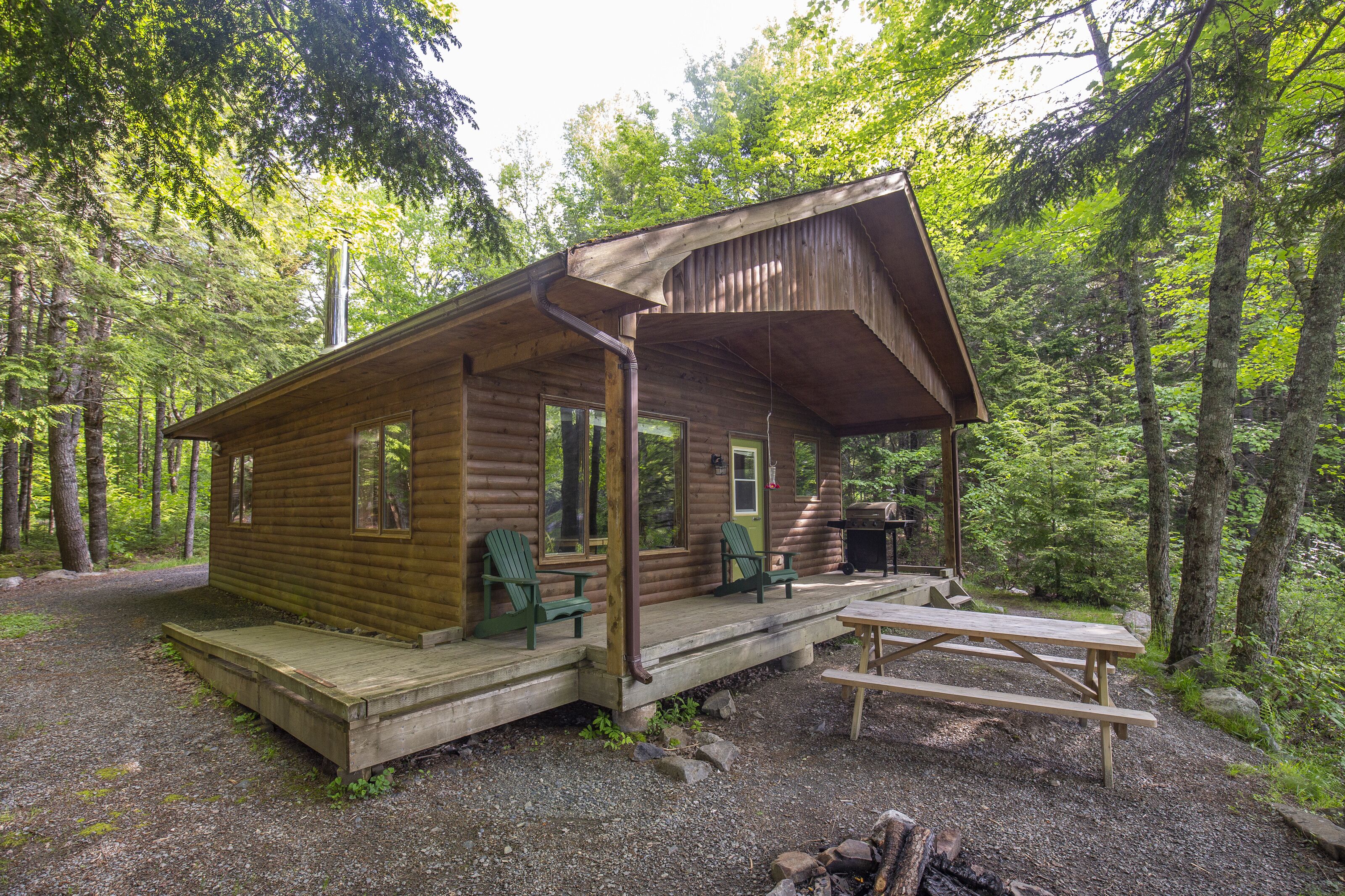 Een rustieke hut met een veranda, twee groene stoelen en een picknicktafel.