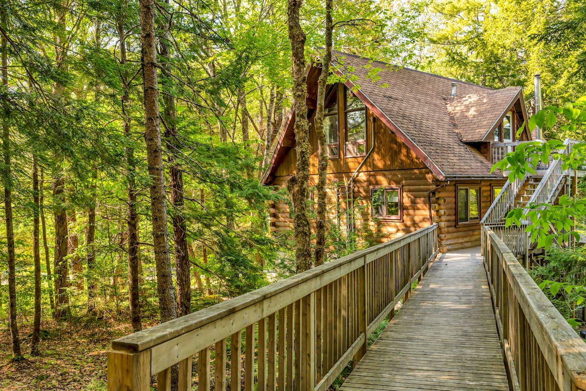 Eine Holzhütte mit Terrasse und Treppe, umgeben von dichtem Wald.