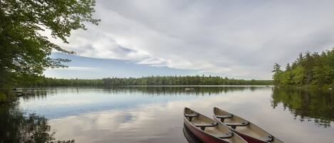 A calm lake with two canoes tied to a dock, surrounded by dense forest.