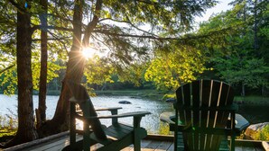 A wooden deck with Adirondack chairs overlooking a lake, surrounded by trees and greenery. - Mersey River Chalets a nature retreat (Maitland Bridge)