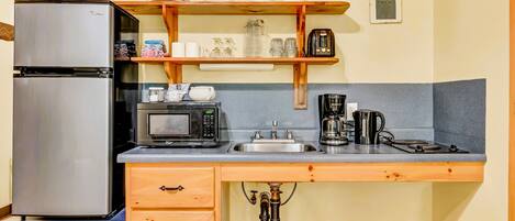 A compact kitchen with a stainless steel refrigerator, a microwave, a coffee maker, and a sink.