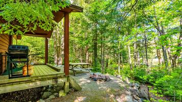 A wooden deck with a grill and picnic table, surrounded by a forest.