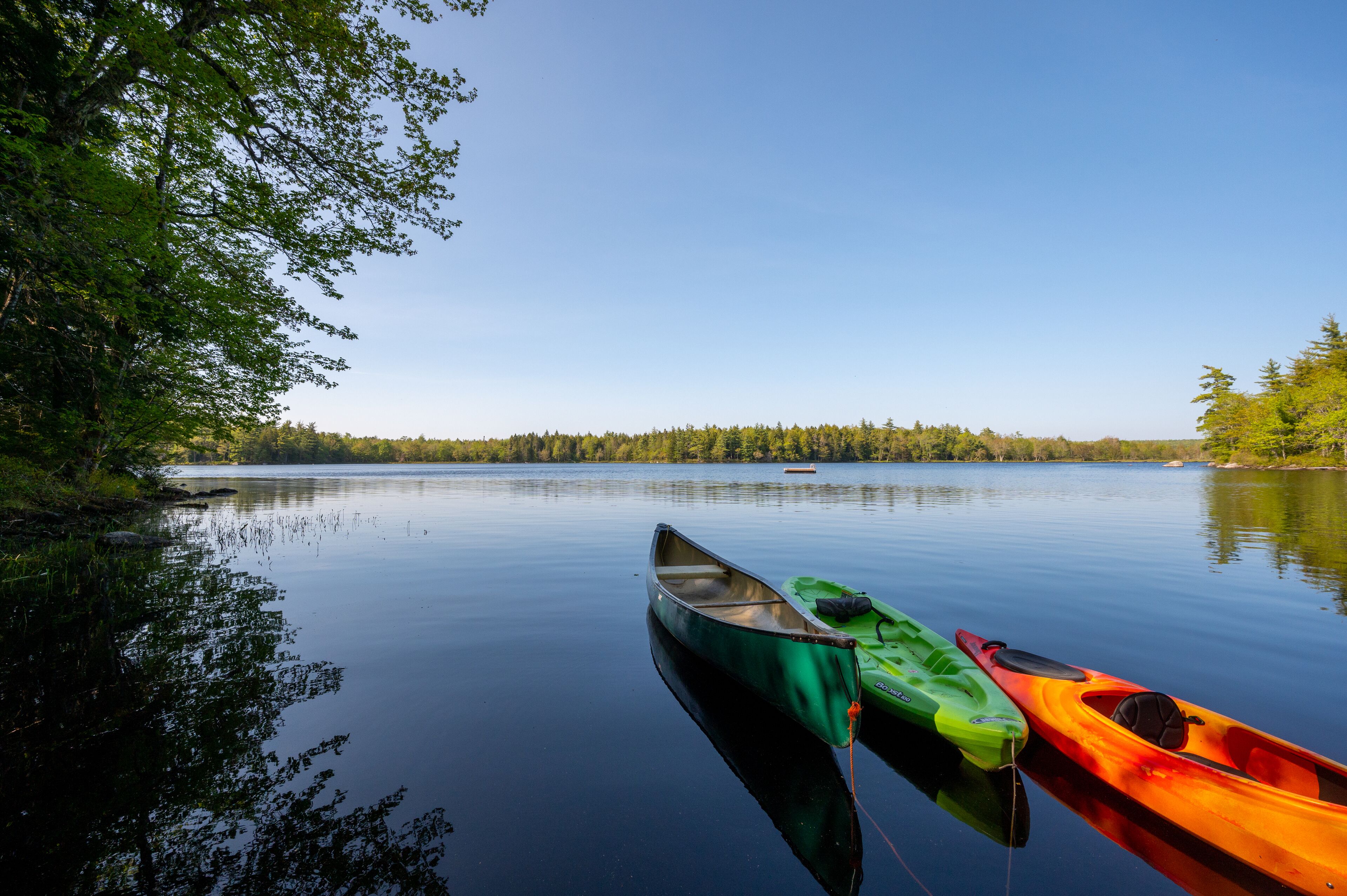 A calm lake with three kayaks docked on the shore.