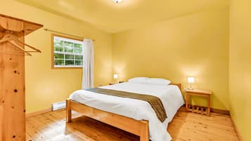 A bedroom with a wooden bed, a bedside table with a lamp, and a window with curtains.
