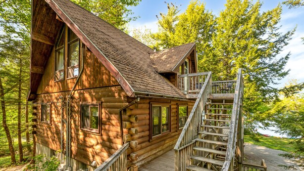 A log cabin with a wooden staircase leading to a deck, surrounded by trees. - Mersey River Chalets a nature retreat (Maitland Bridge)
