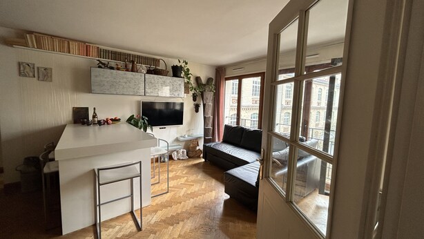 Eine moderne Küche mit einer weißen Kochinsel, einem integrierten Fernseher und einem Essbereich mit einer Couch und einem großen Fenster.