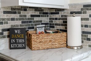 A kitchen with a sign that reads "WE DANCE IN THIS KITCHEN," a woven basket, and a paper towel holder.