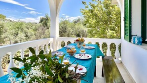 A covered outdoor dining area with a table set for two, overlooking a lush garden. - Astra Beach House in Astrakeri Bay (Astrakeri)