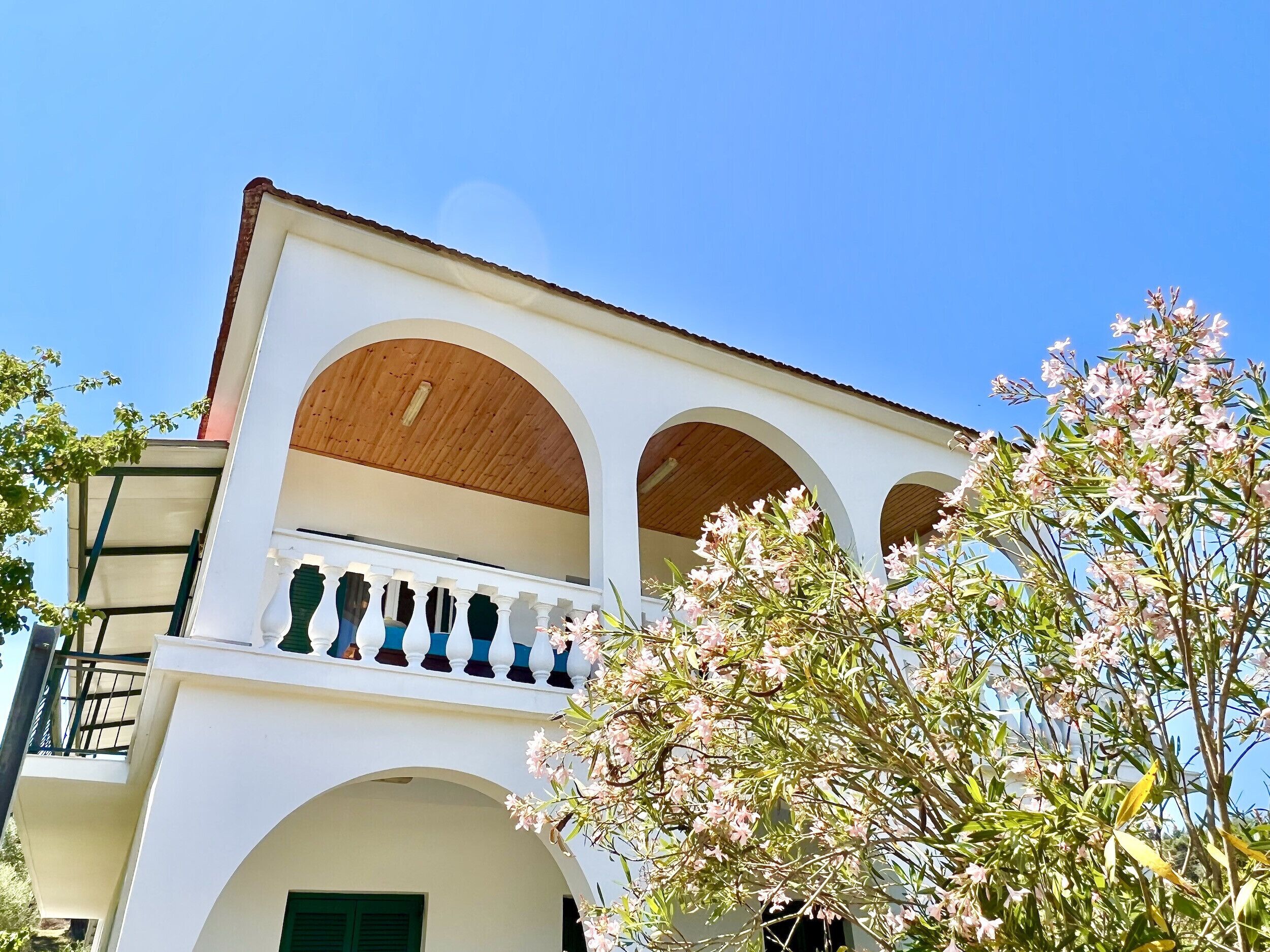 Edifici de dues plantes amb façana blanca, sostre de fusta i un balcó amb barana blava.