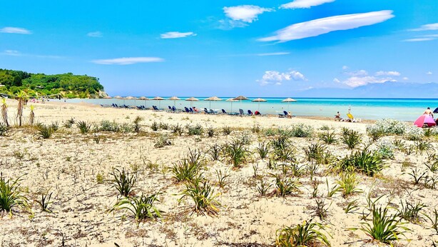 A beach with rows of sun loungers and umbrellas, a clear sky, and a distant view of the sea. - Astra Beach House in Astrakeri Bay (Astrakeri)
