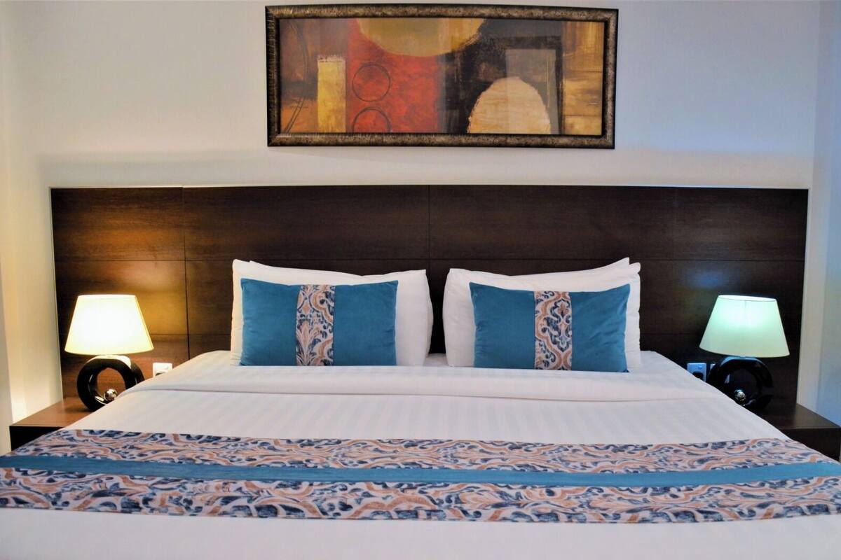 Una cama bien hecha con un edredón estampado, dos almohadas a juego y un cuadro abstracto enmarcado encima.