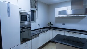 A modern kitchen with white cabinets, a stainless steel range, a built-in oven, a microwave, a sink, and a black countertop. - Butterfly Residence (Manama)