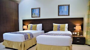 A hotel room with two beds, each with a patterned bedspread and matching pillows. There are two bedside tables with lamps, a large dark wood headboard, and two framed pictures on the wall. - Butterfly Residence (Manama)