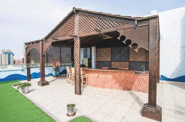 Un bar situé sur le toit d’un immeuble, doté d’une pergola en bois, de sièges et offrant une vue sur le panorama urbain.