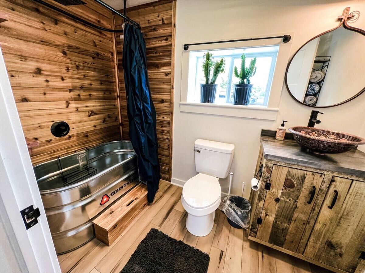 Ein kleines Badezimmer mit Holzwand, Toilette in Weiß, Waschbecken mit dekorativer Schale und Fenster mit Blumentöpfen.