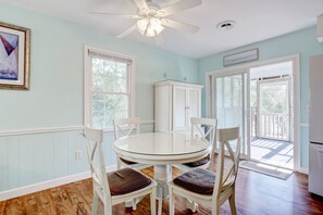 A dining area with a round glass table, white chairs, a ceiling fan, and a view through the glass doors.
