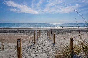 Walk along the beach to the ocean, where a wooden fence and rope barrier lead the way.